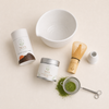 Flat-lay of the NOA Matcha complete organic set — tin, bowl, whisk, holder and sifter with sifted matcha